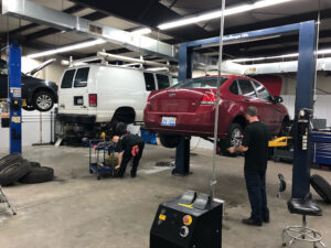 Two mechanics working on a white van and maroon car inside Pete's Garage in Durham